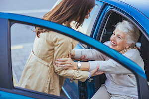 Old person being helped out of a blue car by a younger woman