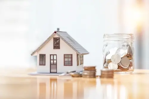 Model of a house next to a jar of coins