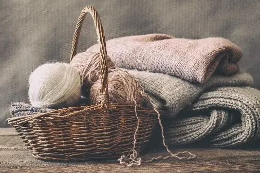 Balls of yarn in woven basket with knitted jumpers