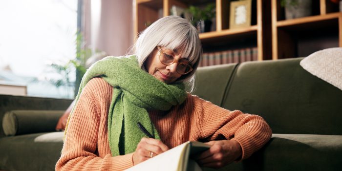 Older woman writing inside with a green scarf on