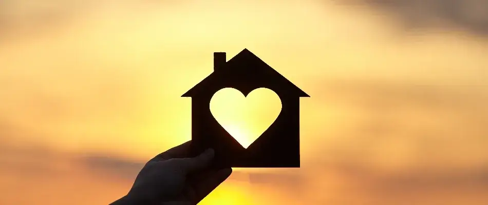 Model home with heart cutout held up in the sunset