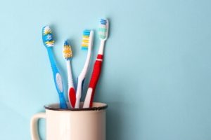 White cup filled with four different coloured toothbrushes against a blue background