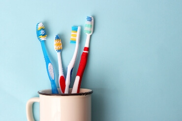 White cup filled with four different coloured toothbrushes against a blue background
