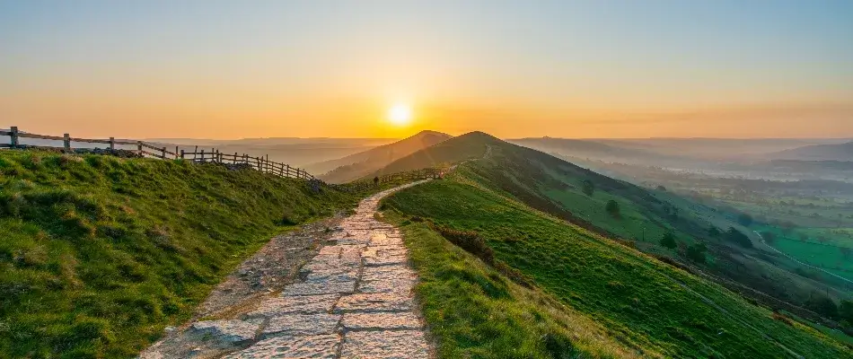 Stone pathway surrounded by green hills against a sunrise